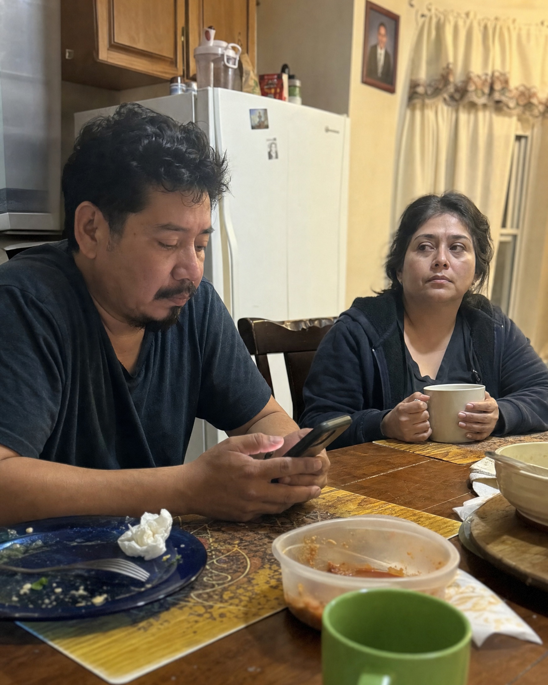 Una pareja sentada a la mesa mientras el esposo mira su teléfono